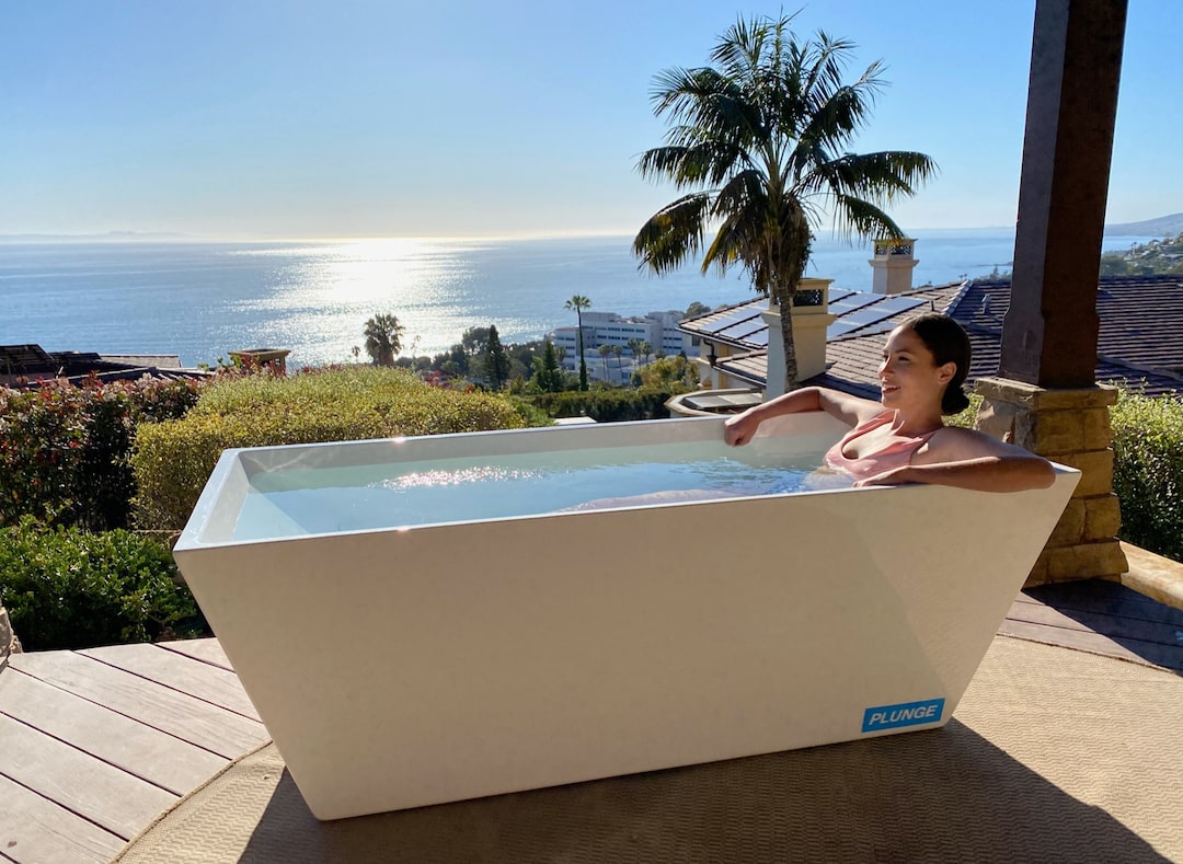 A woman sitting in a PLUNGE cold tub, overlooking the ocean