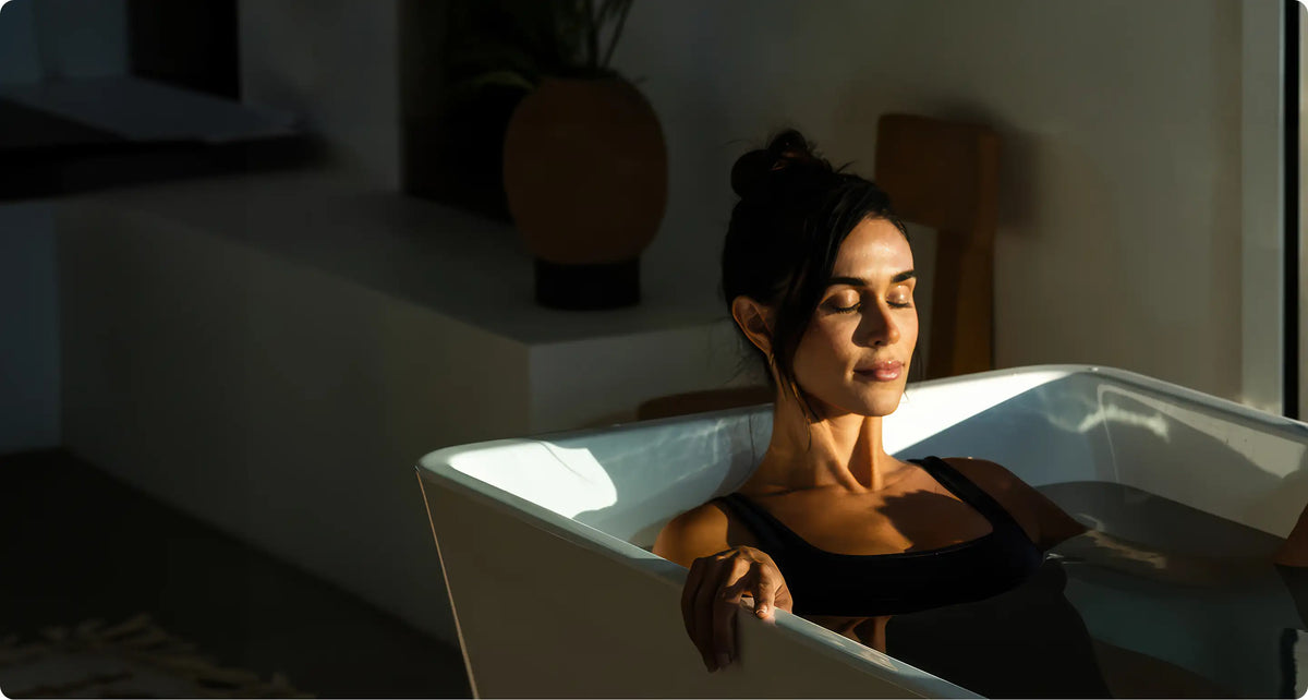 A woman relaxing in a white Plunge cold tub in a sunlit room.