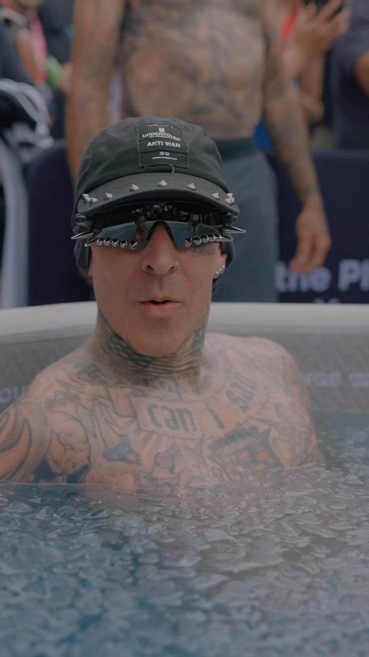 Tattooed person wearing spiked sunglasses and hat, sitting in a pool.