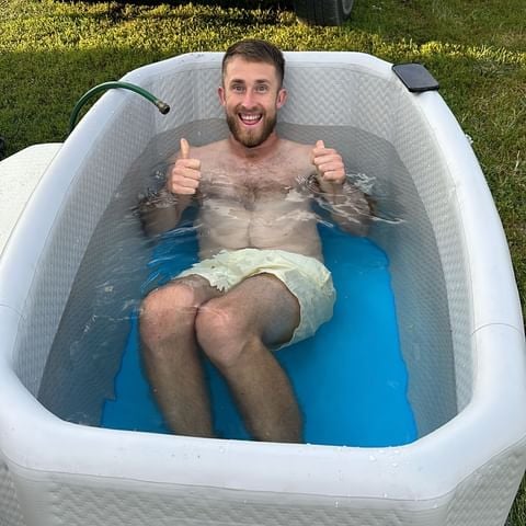 Man relaxing in an outdoor inflatable tub, giving a thumbs-up.