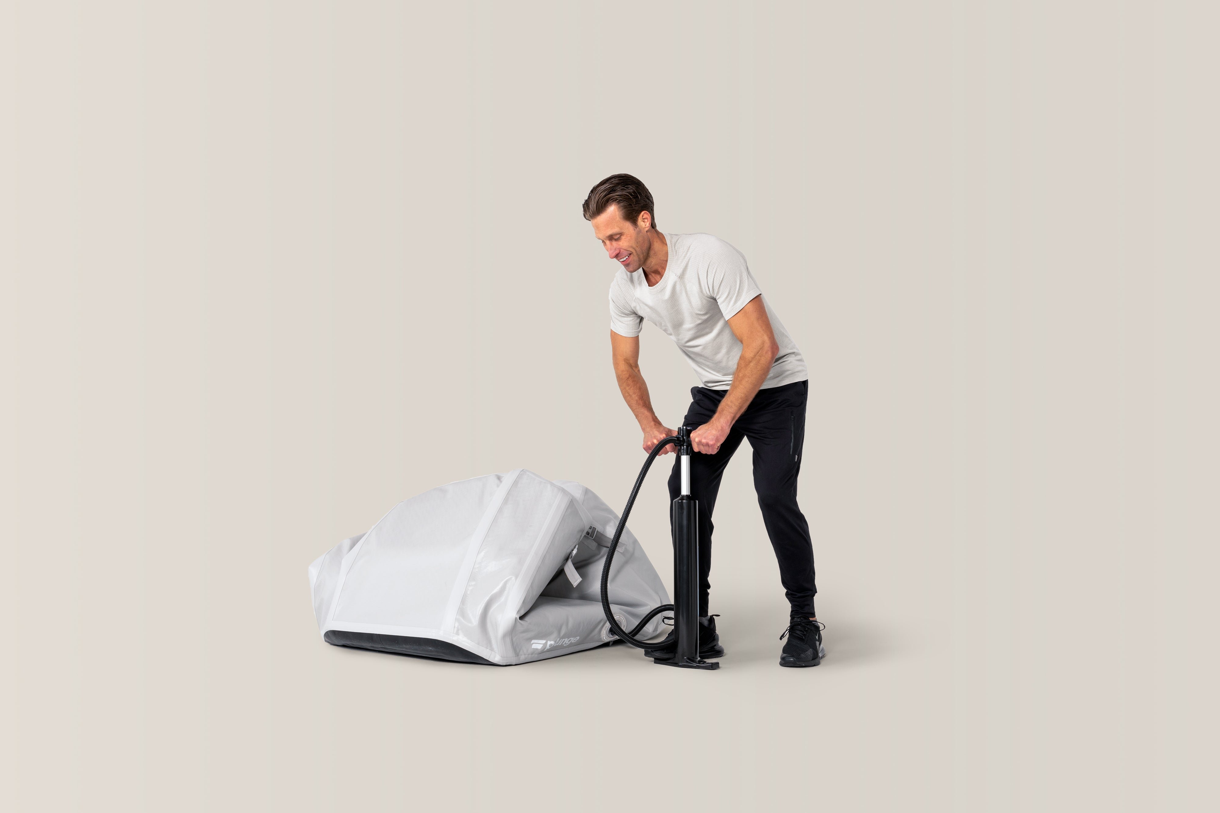 A man inflates a grey portable shelter with a manual pump.