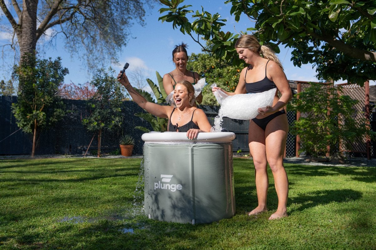 Three women enjoying an ice bath in a portable tub outdoors.
