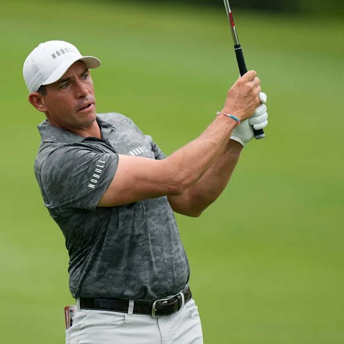 Golfer in a gray shirt and white cap swinging a club on a golf course.