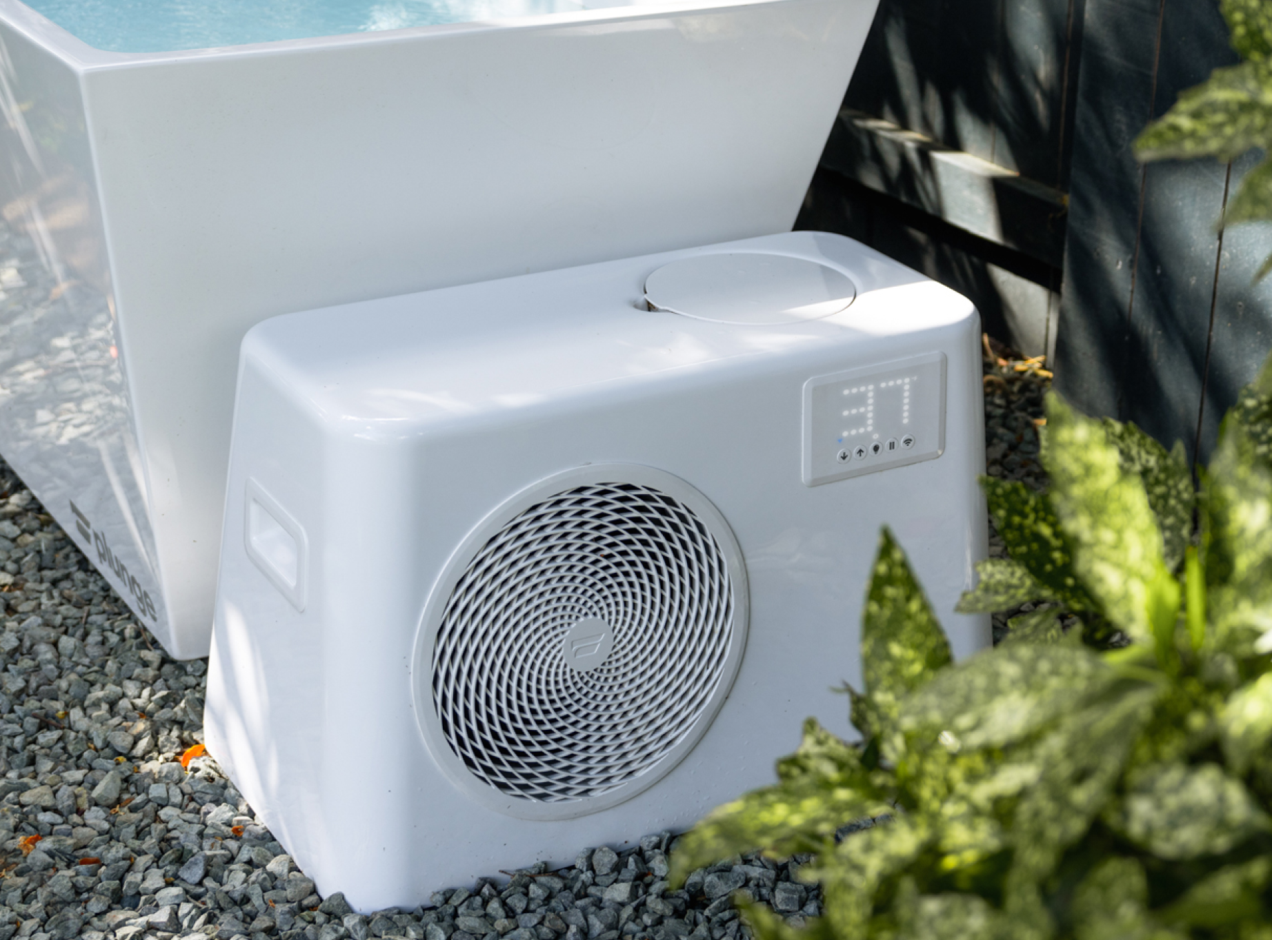 Outdoor white air conditioning unit set against a gravel ground and plants.