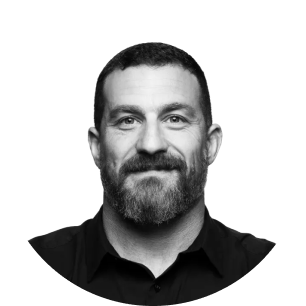 A man with a beard and short hair smiling in a circular black and white photo.