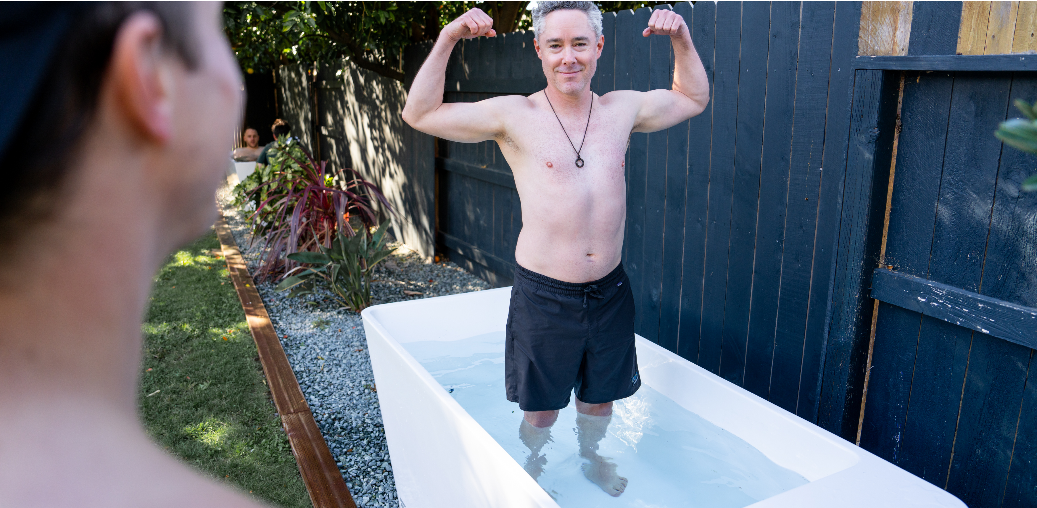 Man flexing his muscles while standing in an outdoor bathtub.