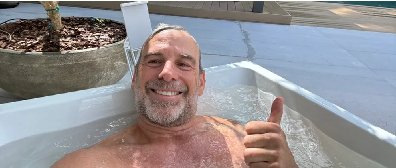 Man smiling and giving thumbs up while relaxing in an outdoor hot tub.
